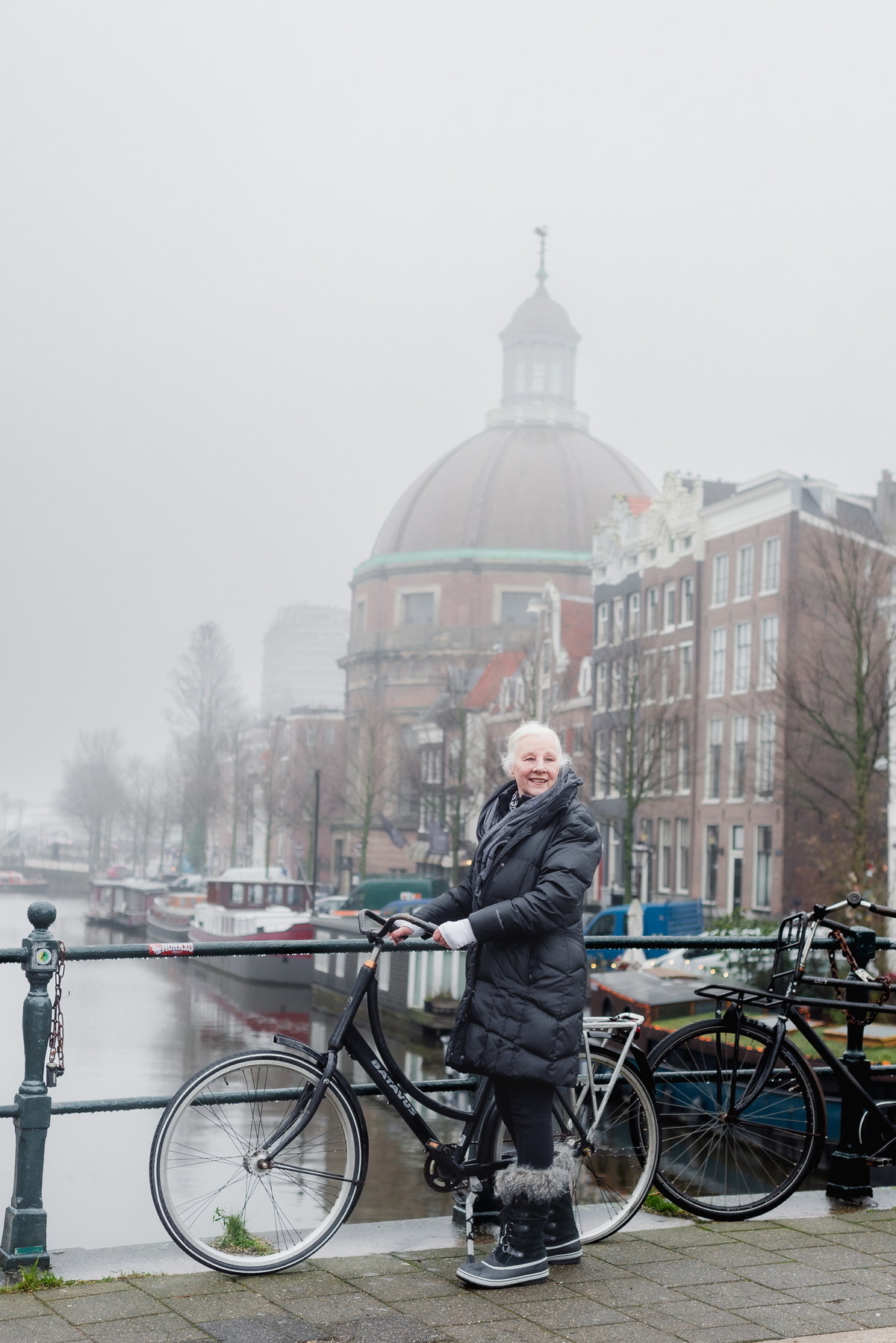 Woman in a birthday sash standing beside a canal with a church tower in the mist behind her.