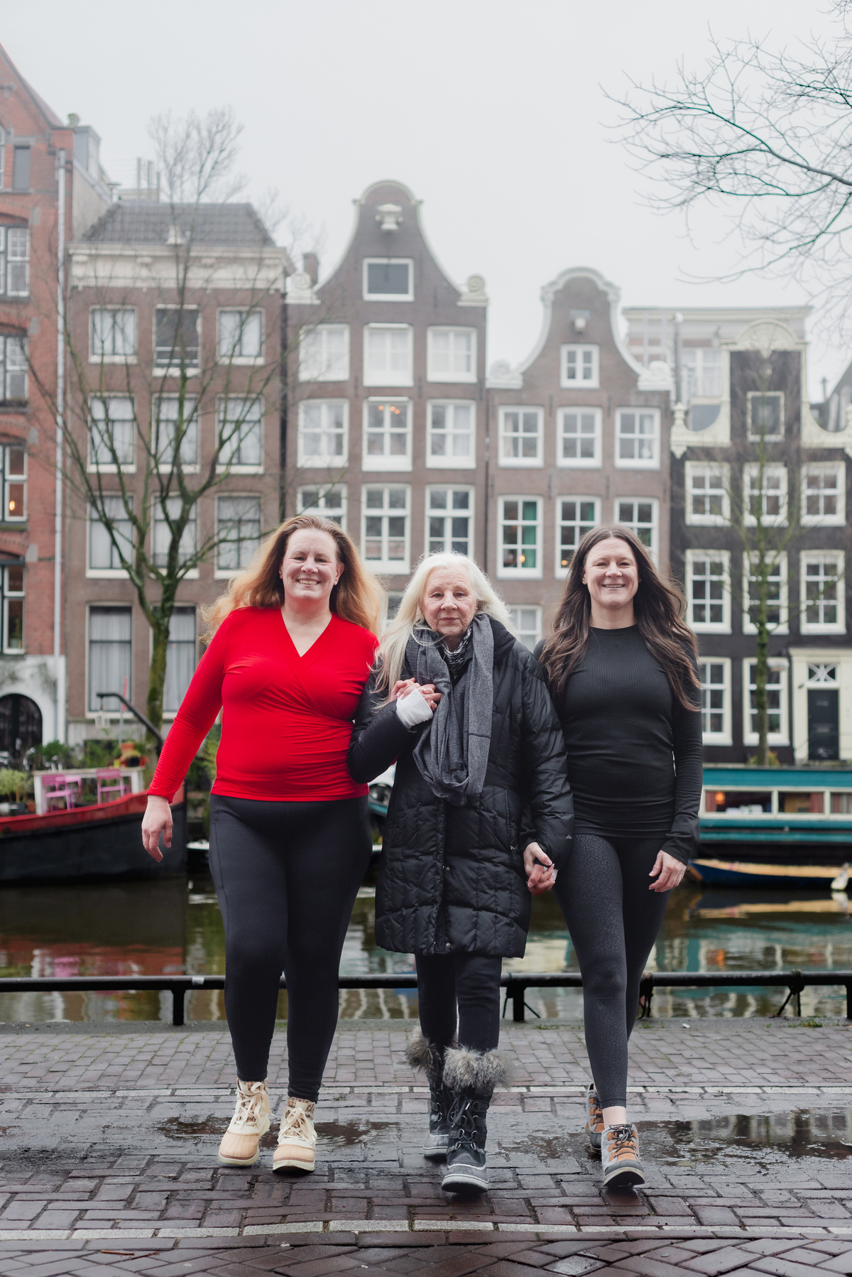 Three women standing together beside an Amsterdam canal in soft winter light.