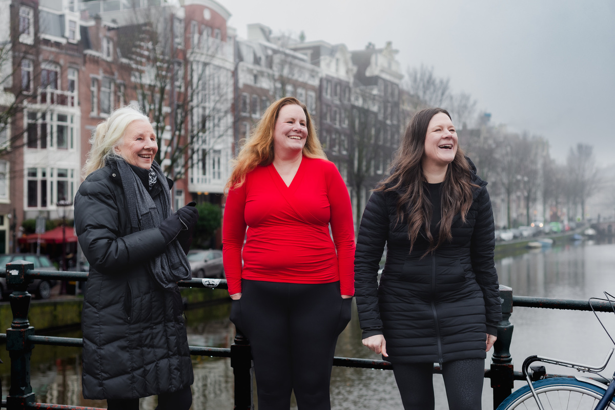 Three women standing together on a canal bridge in Amsterdam.