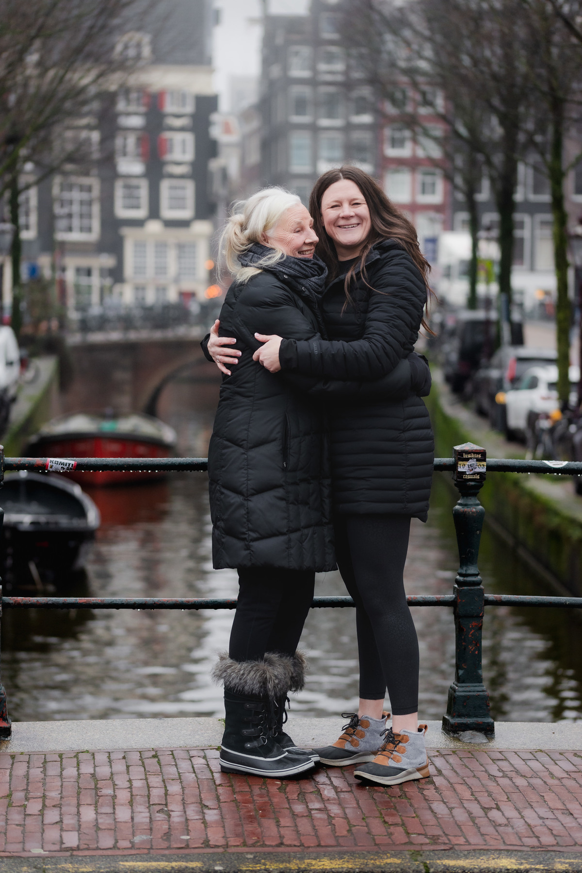 Two women standing together beside an Amsterdam canal on a foggy winter morning.