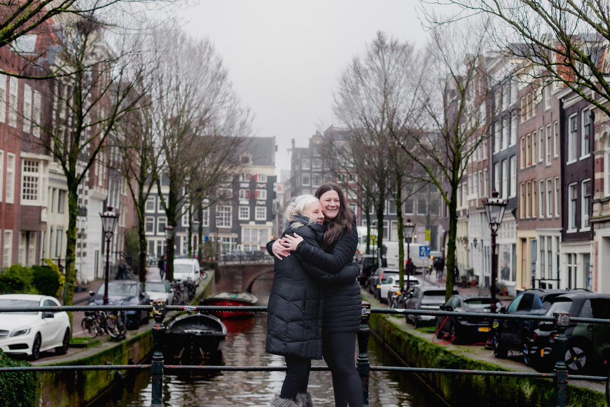 Family members hugging on a canal bridge during a 70th birthday celebration in Amsterdam.