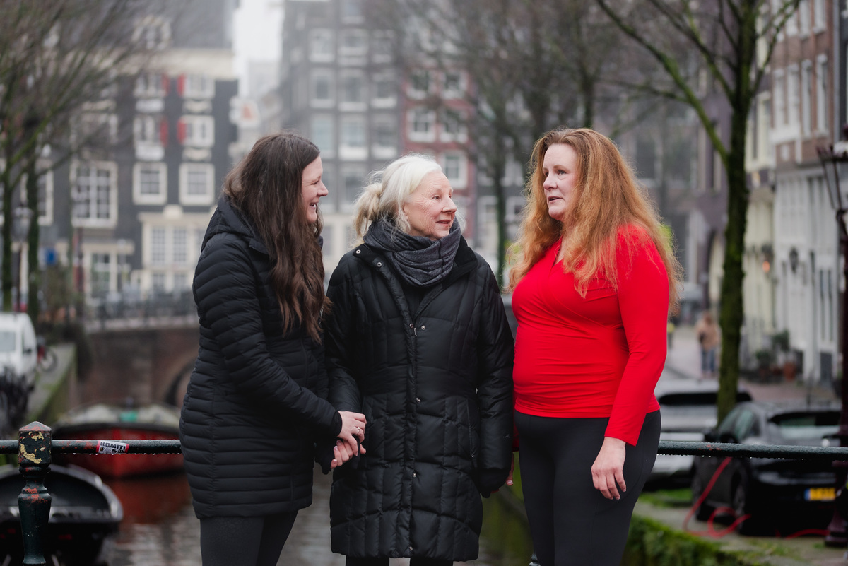 Family members hugging on a canal bridge during a 70th birthday celebration in Amsterdam.