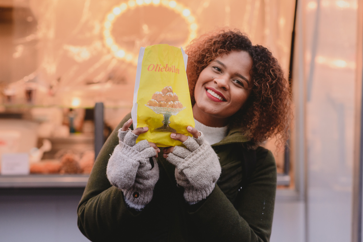 Person holding a paper bag of freshly bought oliebollen at Museumplein in Amsterdam, capturing a quintessential winter treat during a seasonal photo session.