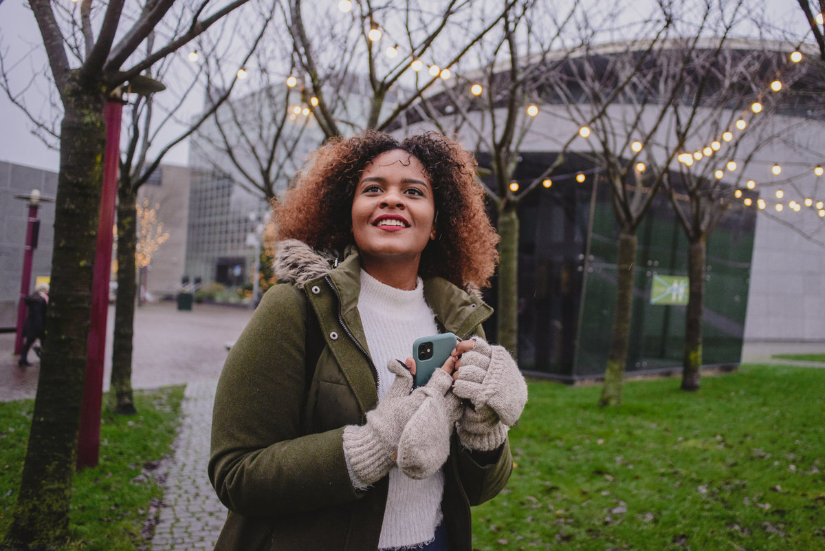 Close-up of a person holding a phone with sparkling Christmas lights glowing softly in the background, adding a festive touch to the photo