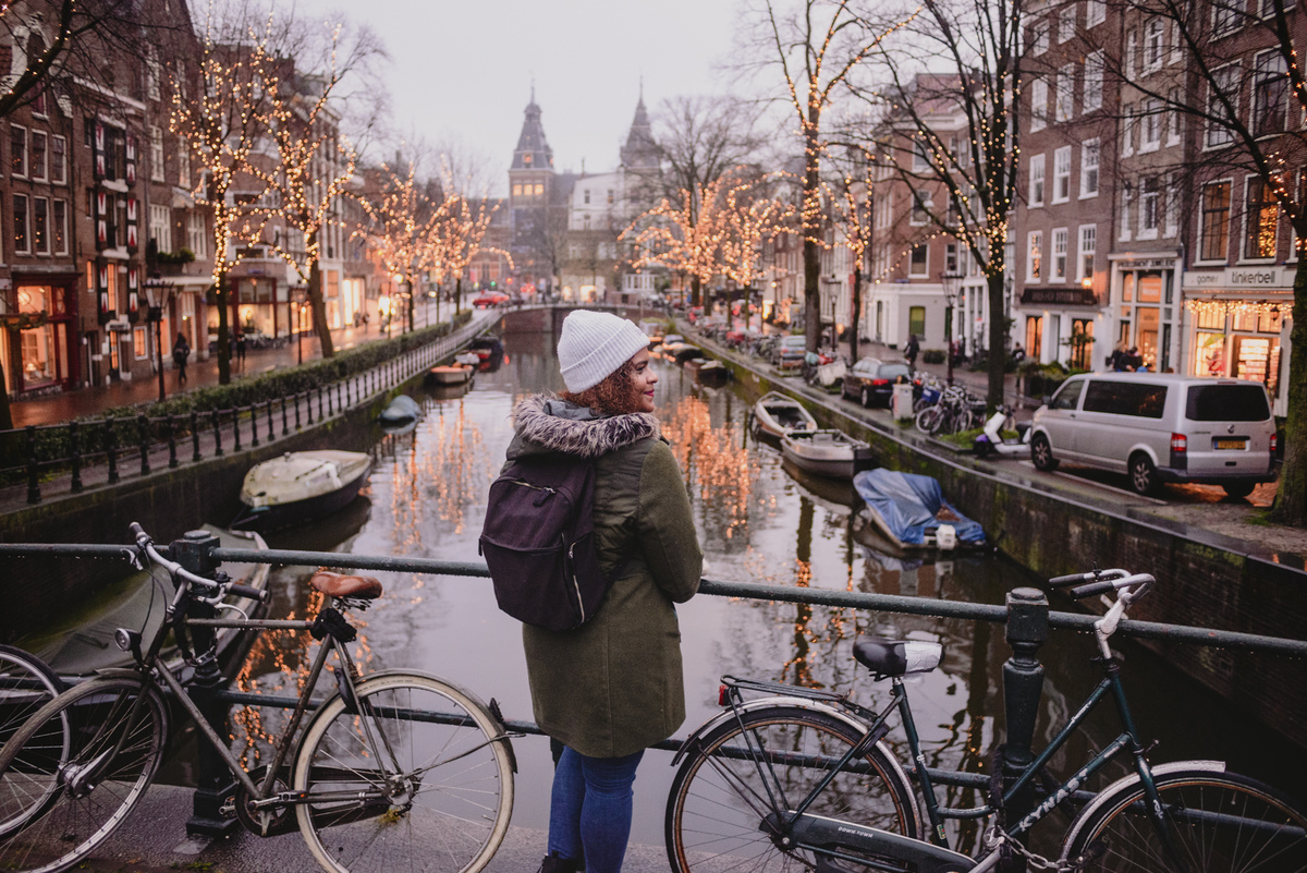 Person standing on a bridge, gazing out over Spiegelgracht, decorated with enchanting winter lights, showcasing the serene beauty of Amsterdam during the colder months.
