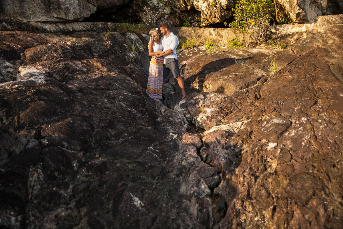 fotos de ensaio, pre wedding dos noivos em Guarujá, noivo abracando a noiva imagem espontanea, Praia das Conchas no Guaruja, São Paulo com as pedras de fundo