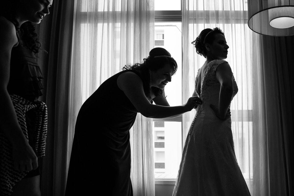 mae da noiva ajudando a fechar o vetido em frente a janela, foto preto e branco