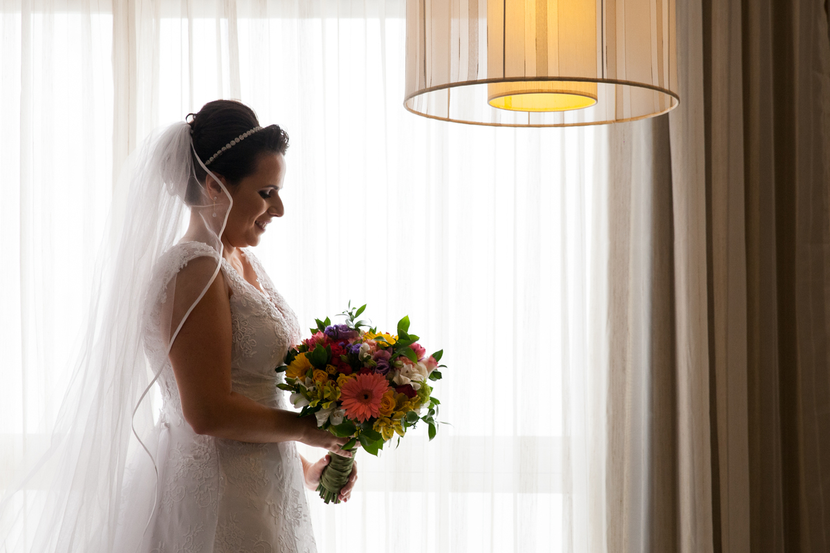noiva pronta de frente a janela olhando para o buque ansiosa para o casamento