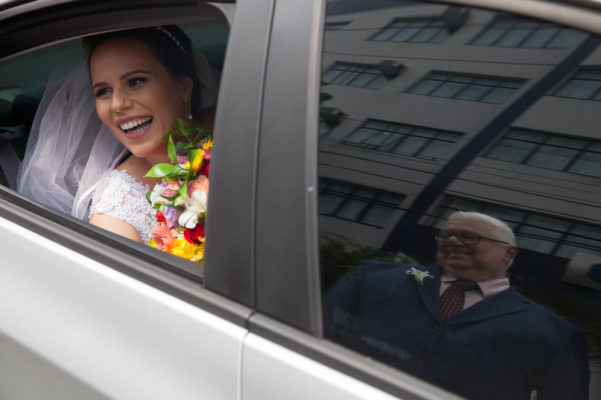Noiva dentro do carro com imagem do pai refletindo no vidro do carro, momento antes da cerimonia de casamento