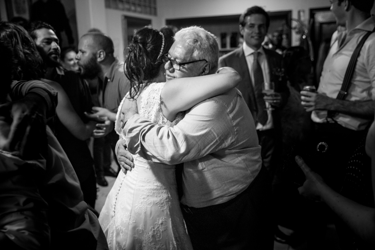 tio da noiva abraca a noiva com o noivo olhando de fundo na festa de casamento na Mansão da Ilha em São Vicente na Ilha Porchat - Sao Paulo - SP