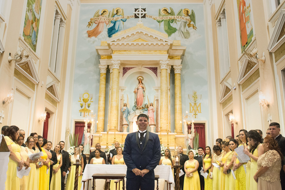 noivo e madrinhas aguardando a noiva entrar com o altar da igreja coracao de maria de fundo