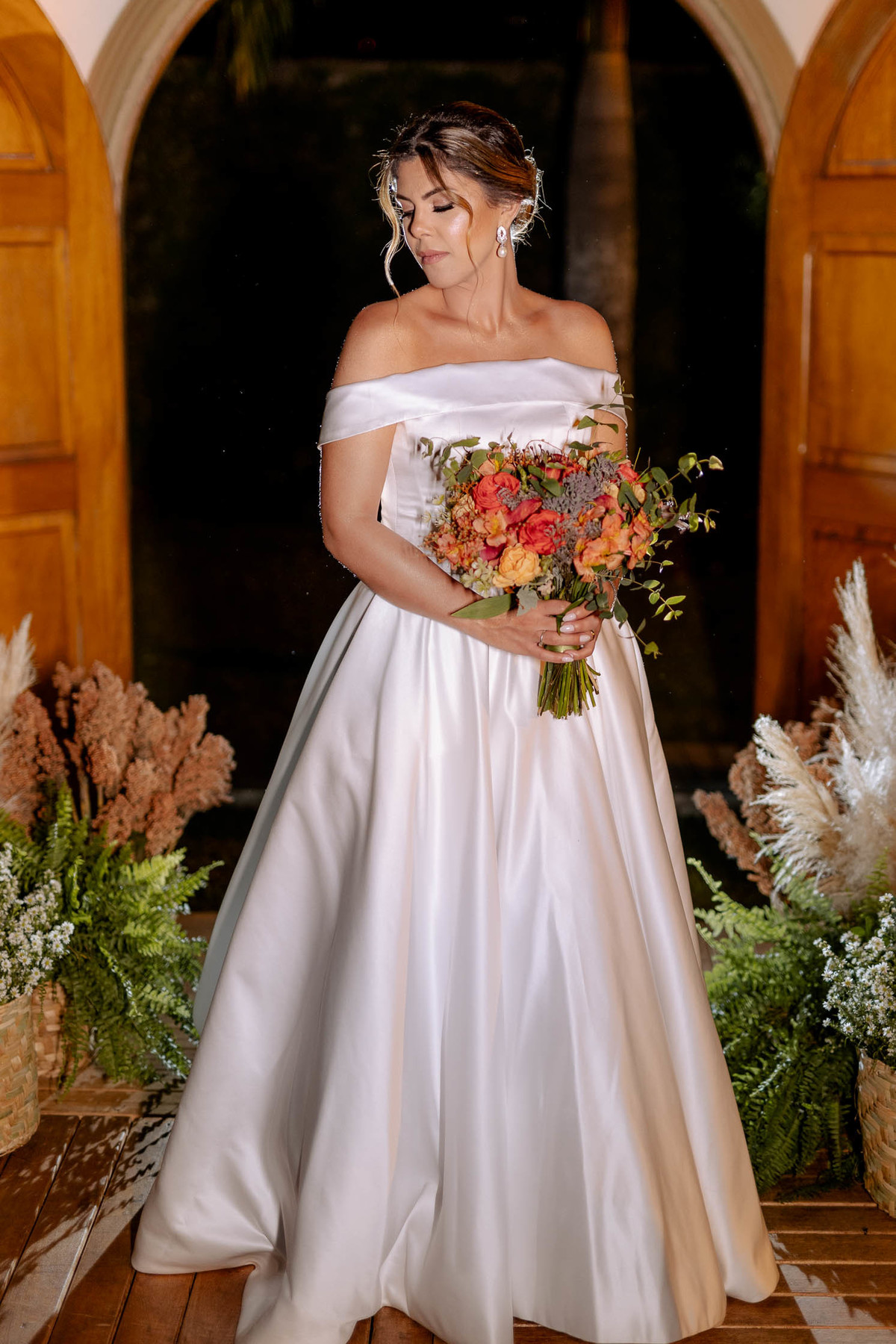 Noiva linda com vestido ombro a ombro e buquê de flores em tons de laranja 