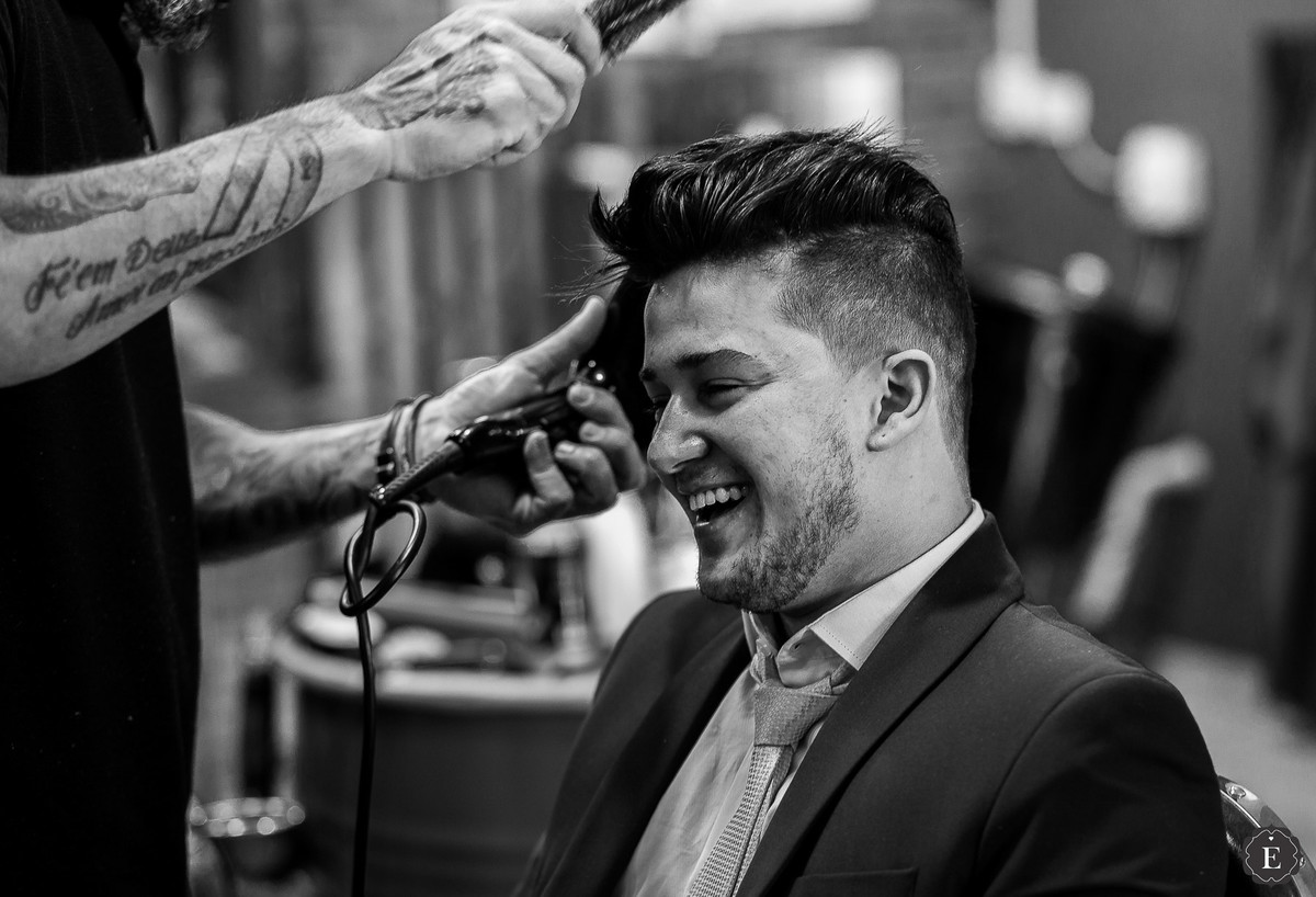 noivo sorrindo e arrumando cabelo para o casamento em fotos na barbearia