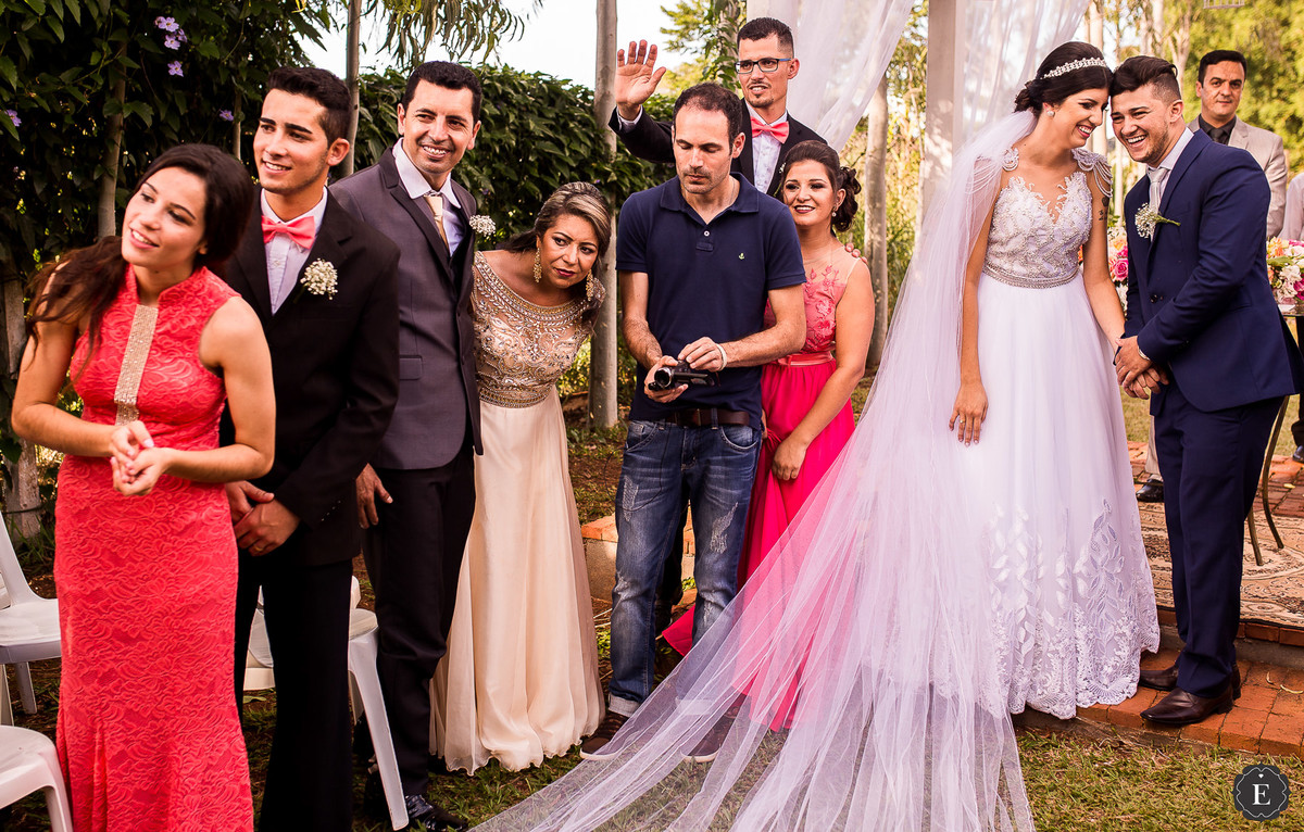 noiva e noivo sorrindo enquanto convidados olham a entrada das alianças