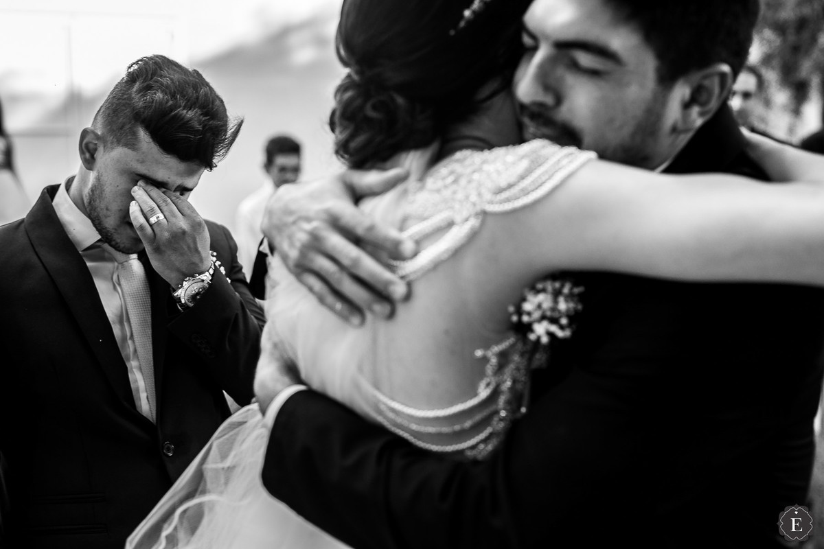 noiva abraçando padrinho enquanto noivo chora