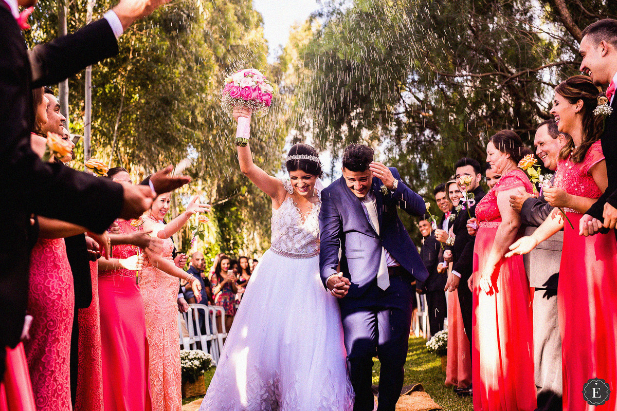 noivos comemorando e padrinhos jogando arroz na saída da cerimônia no campo