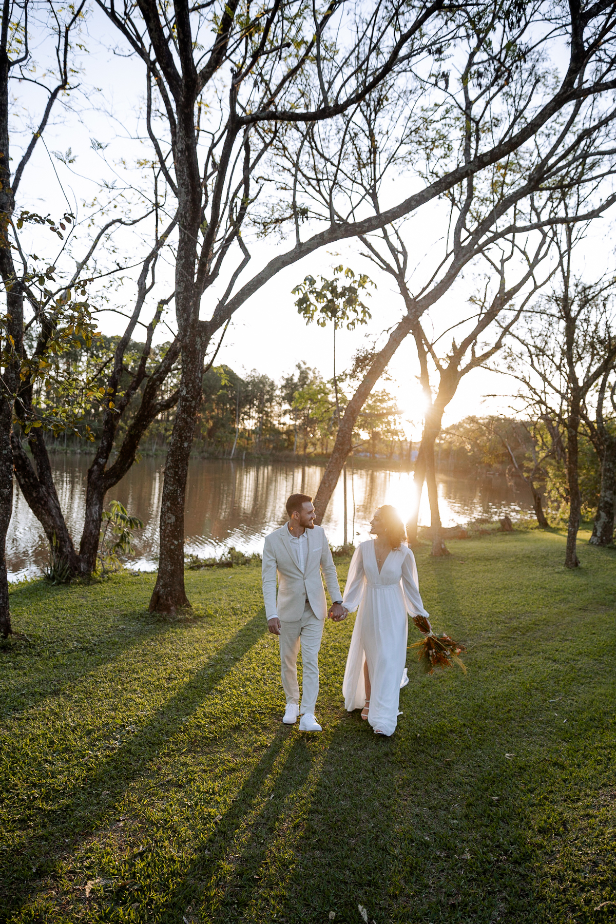 Noivos caminhando em campo com lagoa ao fundo 