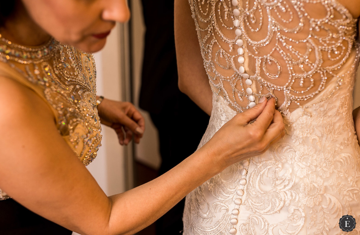 mãe arrumando o vestido da noiva com decote nas costas e bordado