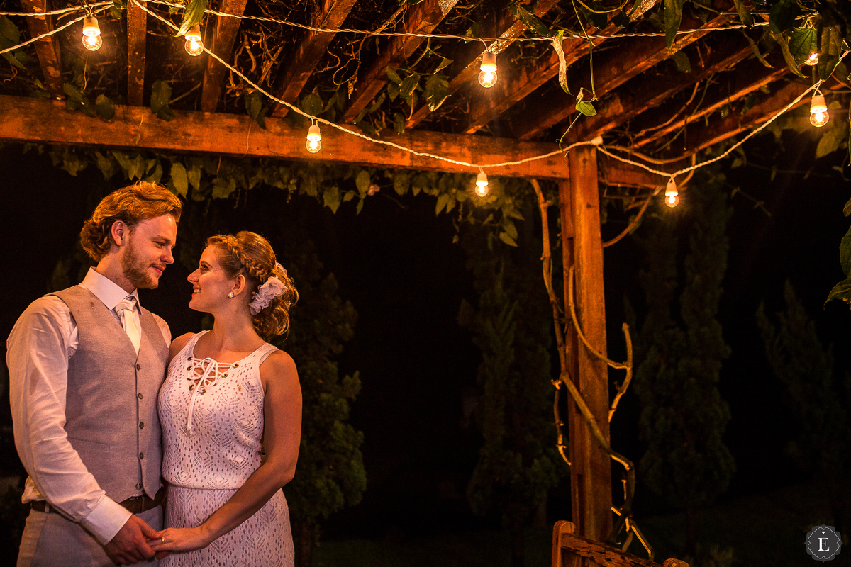 noivos debaixo de pergolado de luzes amarelas em decoração diferente e retro no campo em maringa parana