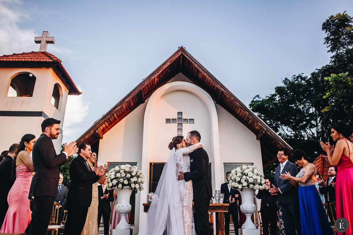 noivo e noiva se beijam no casamento ao ar livre em frente a capela branca