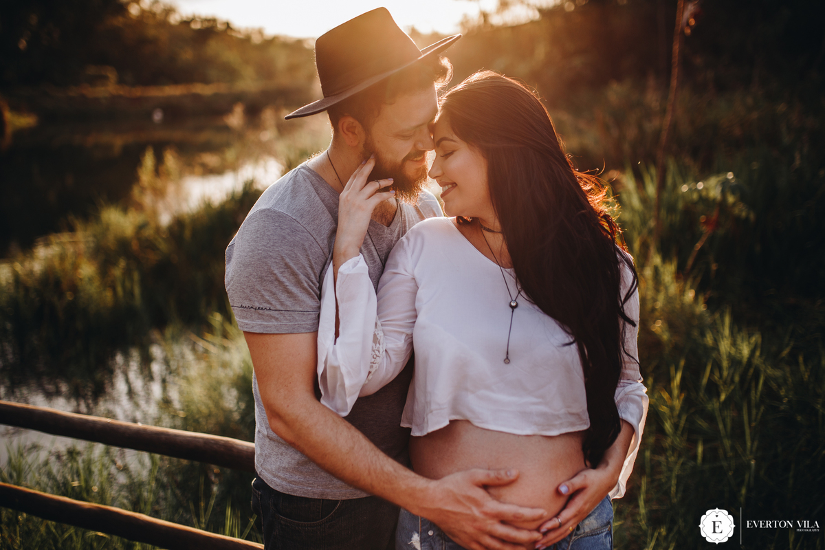 gestante com seu marido usando chapéu vintage na natureza em ensaio fotográfico