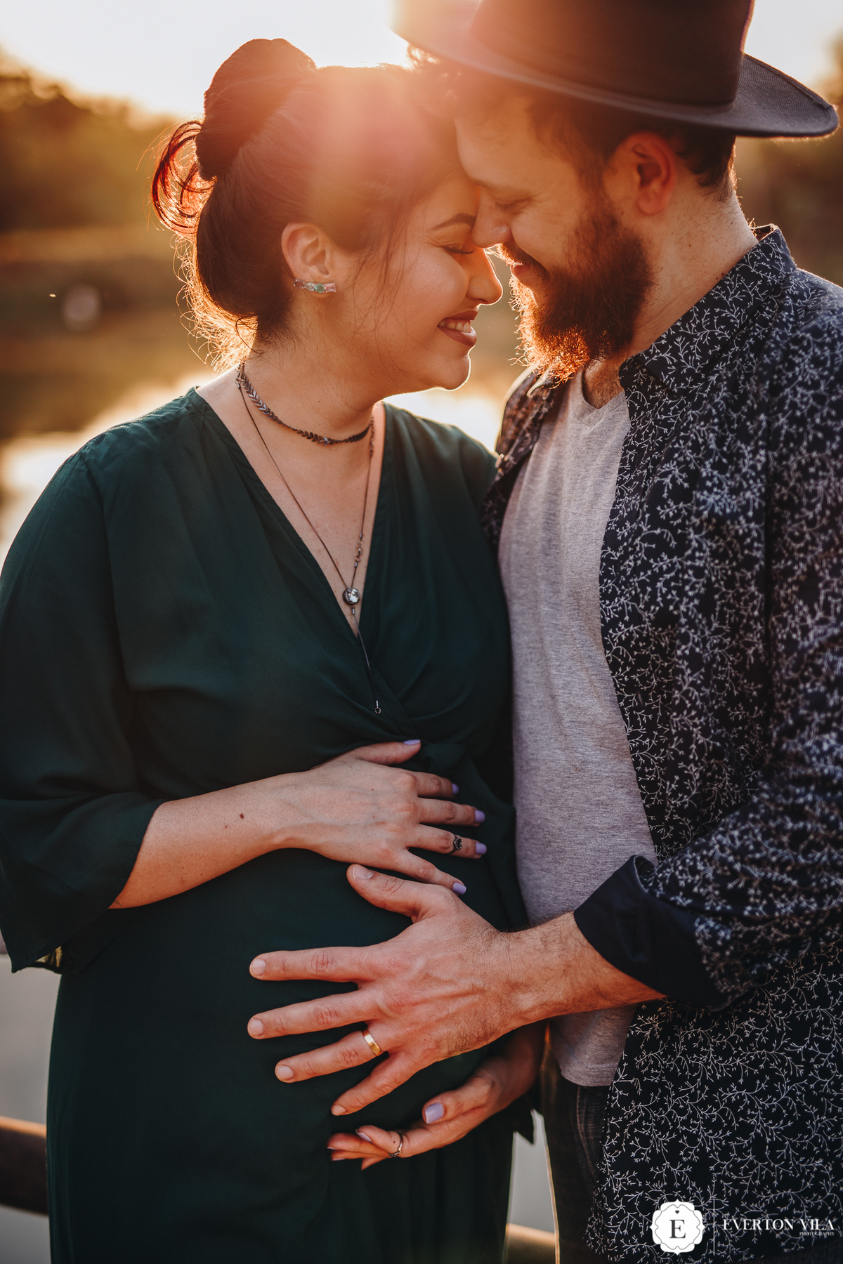 linda gestante usando vestido verde militar abraçada com seu marido em ensaio de fotos 