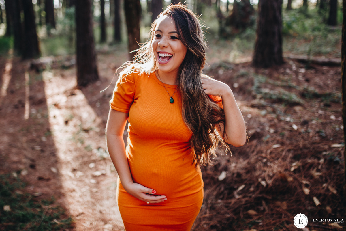 gestante sorridente em sessão de fotos na floresta 