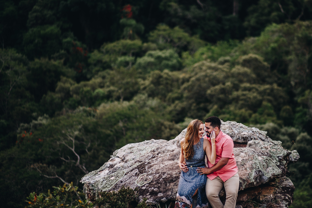 noivos sentados  e abraçados em pedra na floresta