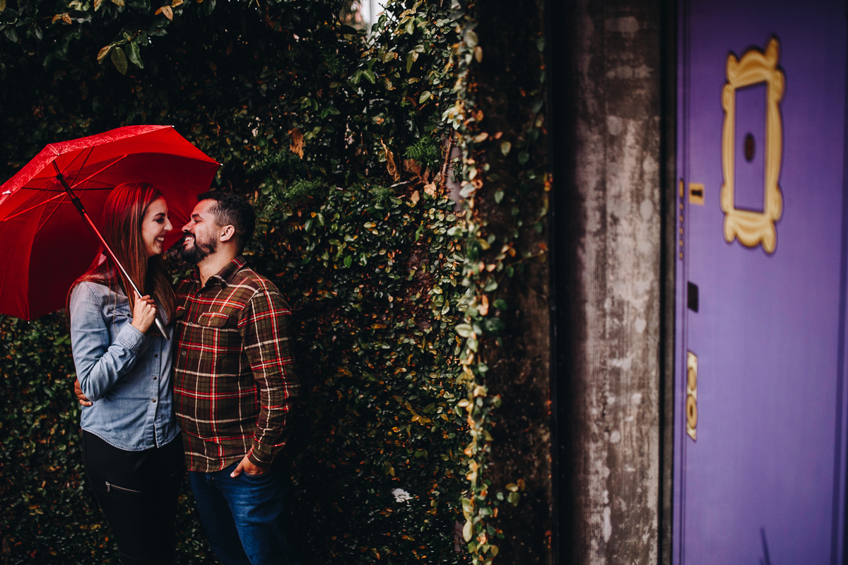 lindo casal abraçados em parede florida com guarda-chuva vermelho