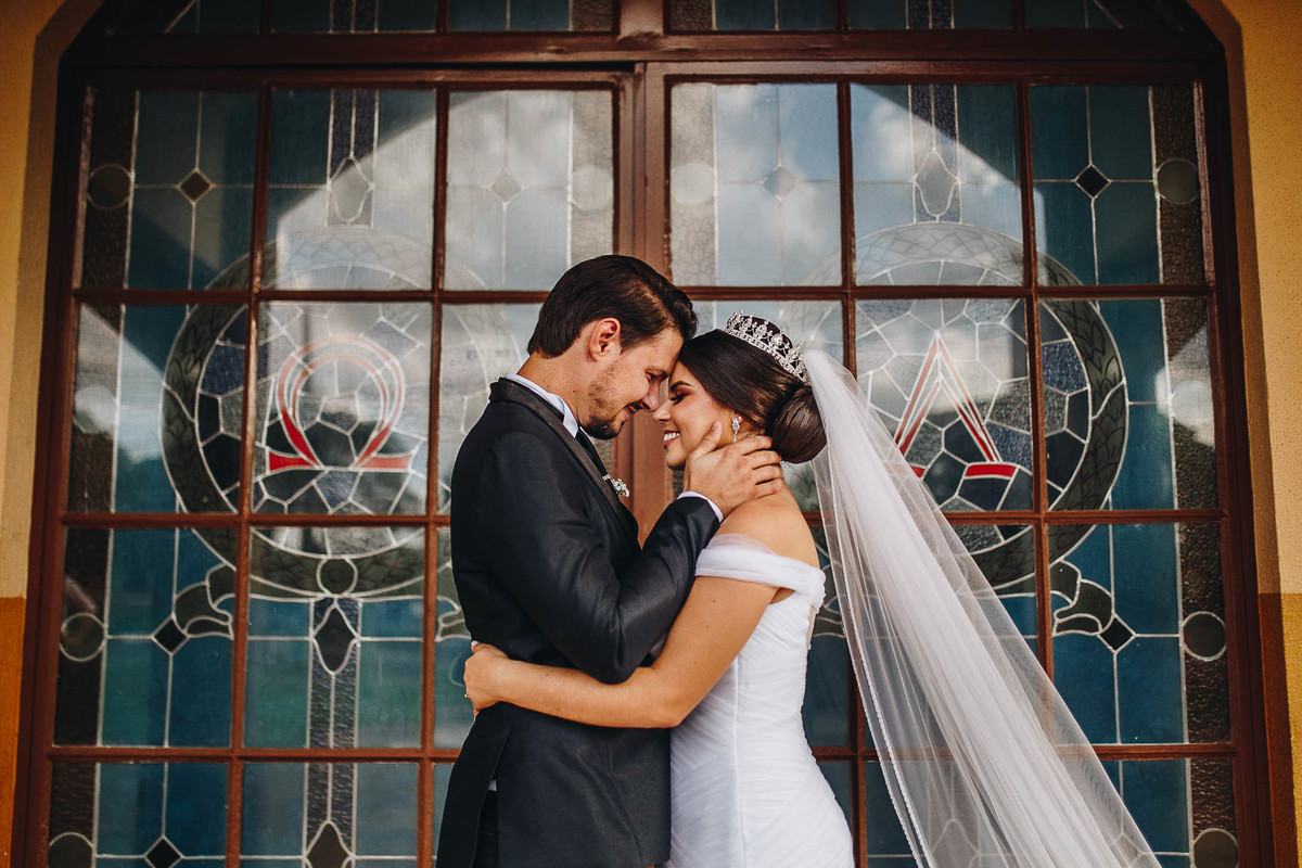 casal de noivos abraçados em porta de vidro linda da igreja 