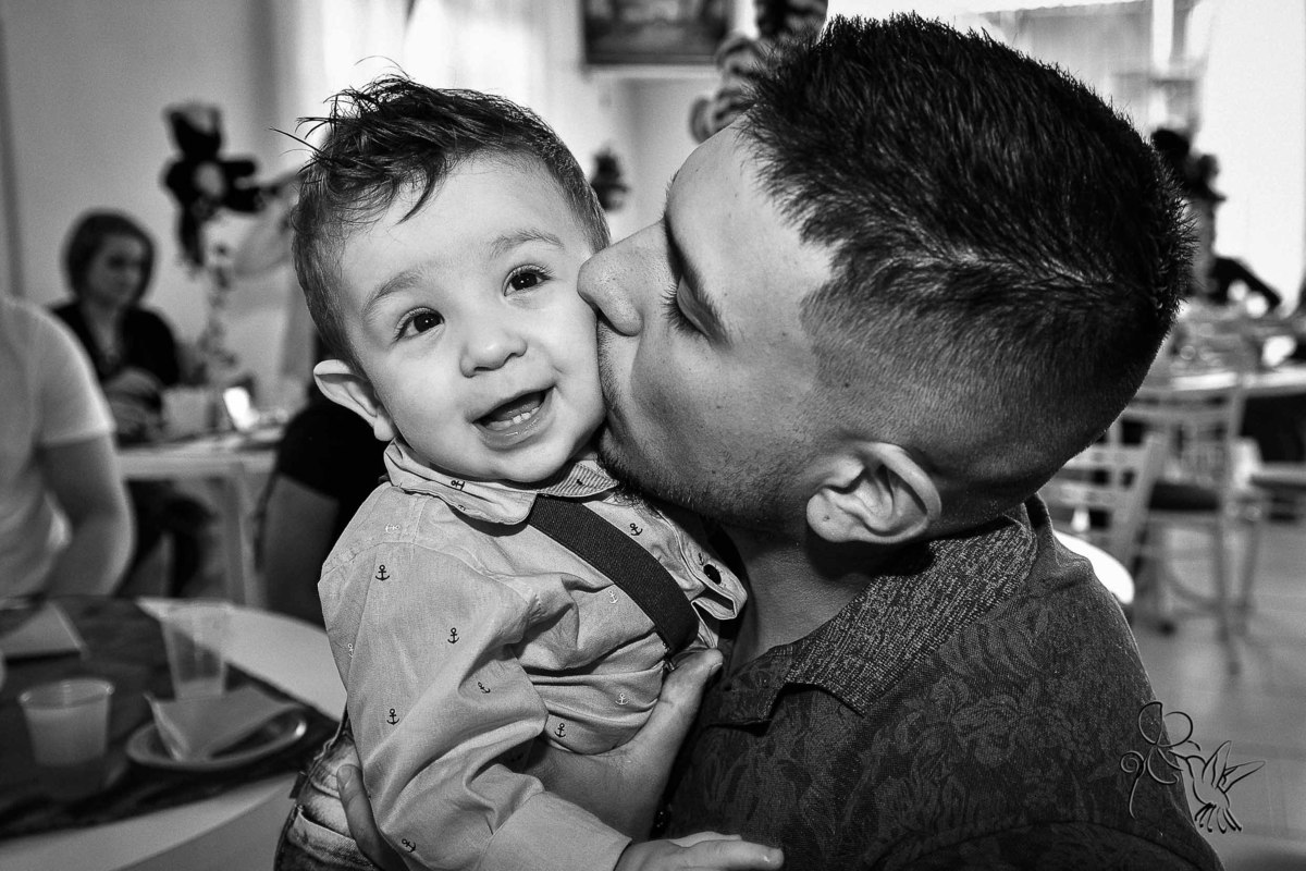 Pai beija o filho de uma aninho no rosto, o bebê sorri. Clique de by Eli Matos.