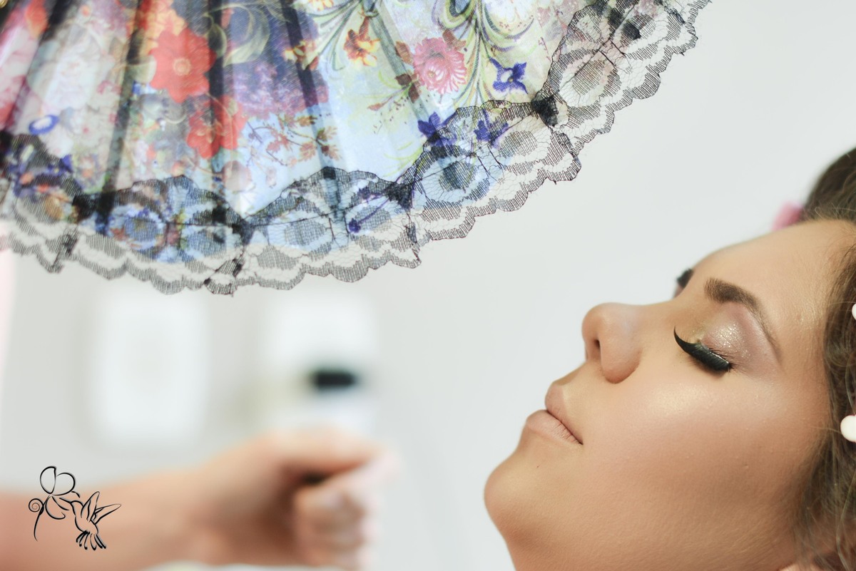 Detalhe de maquiagem de uma noiva, rosto da noiva sendo abanada por um leque colorido, clique de by Eli Matos