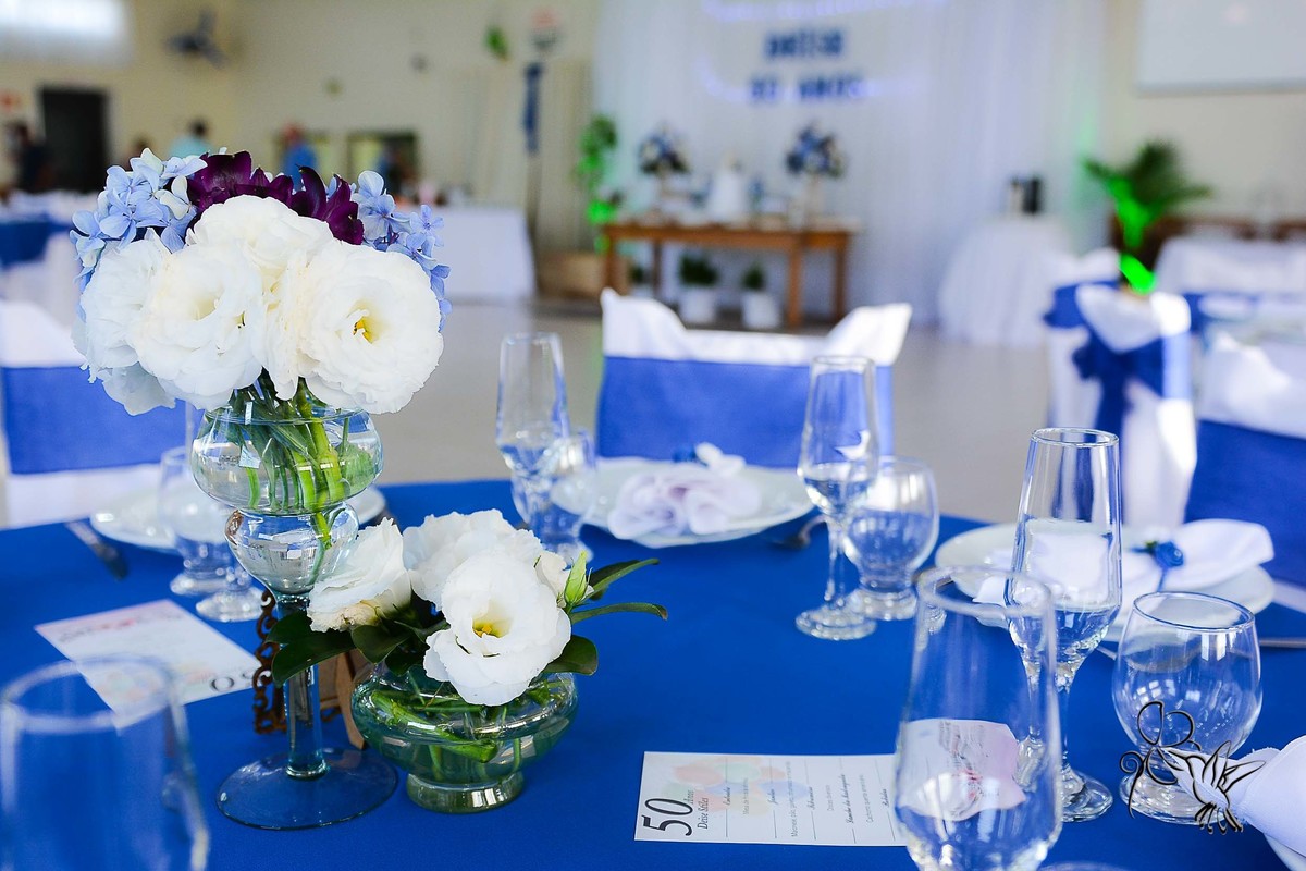 detalhe da mesa, vaso com flores naturais na cor branca, na mesa toalha azul, salão decorado com meses redondas nas cores azul e banco, cadeiras com laços azuis e toalha estampa, by Eli Matos registrou  clicando tudo