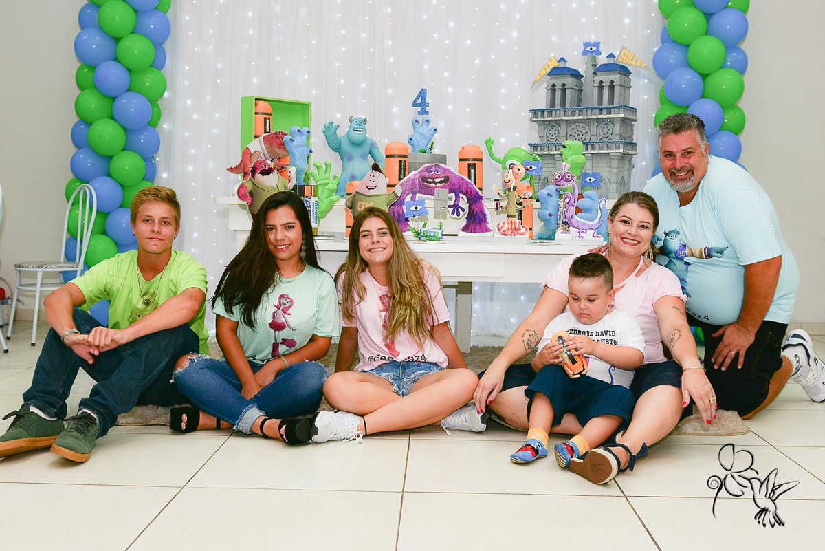 Família de seis pessoas estão sentadas no chão com camisetas coloridas dos personagens do filme Universidade Monstro