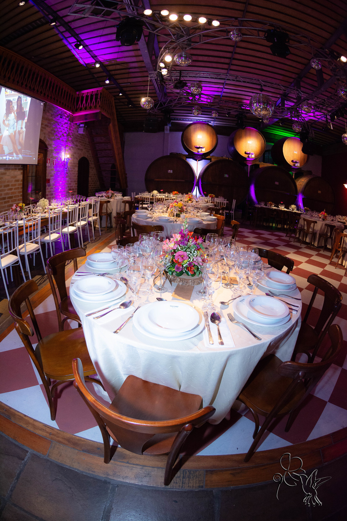 detalhe da mesa decorada para as formandas e ao fundo barris de vinho,  salão dentro de uma catina clicado por de by Eli Matos clicou
