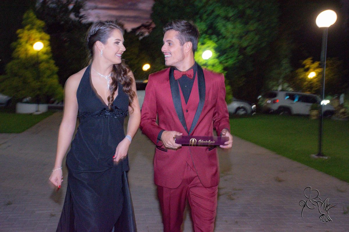 dois jovens caminha alegres para a festa de formatura do rapaz em odotnologia, ele de terno grená e ela de vestido preto, ambos estão muito lindos, by Eli Matos, quem clicou