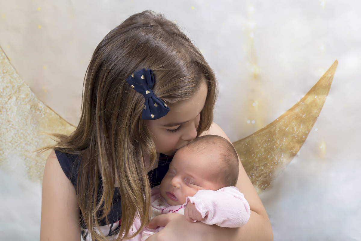 Irmã mais nova a beijar a bebé na sessão fotográfica