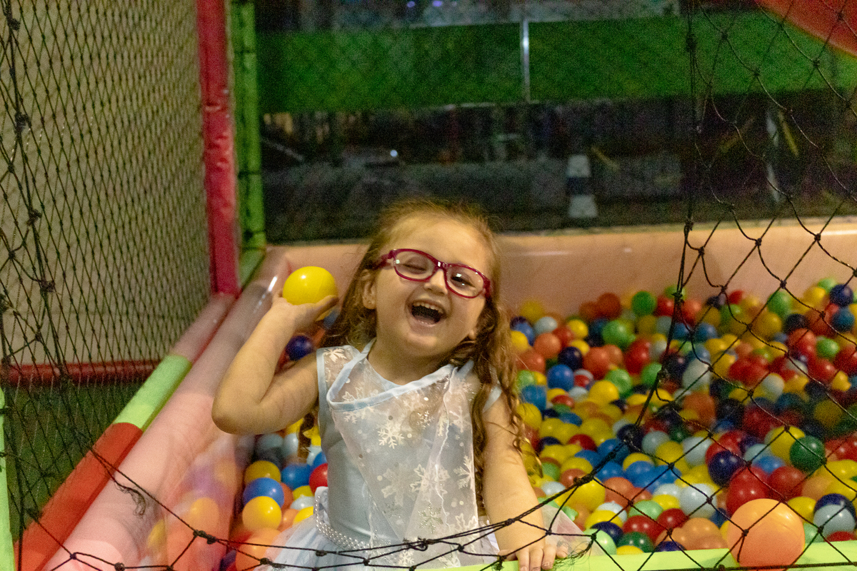 menina dentro de piscina de bolinhas e olhando pra frente pronta para atirar pra fora uma bolinha