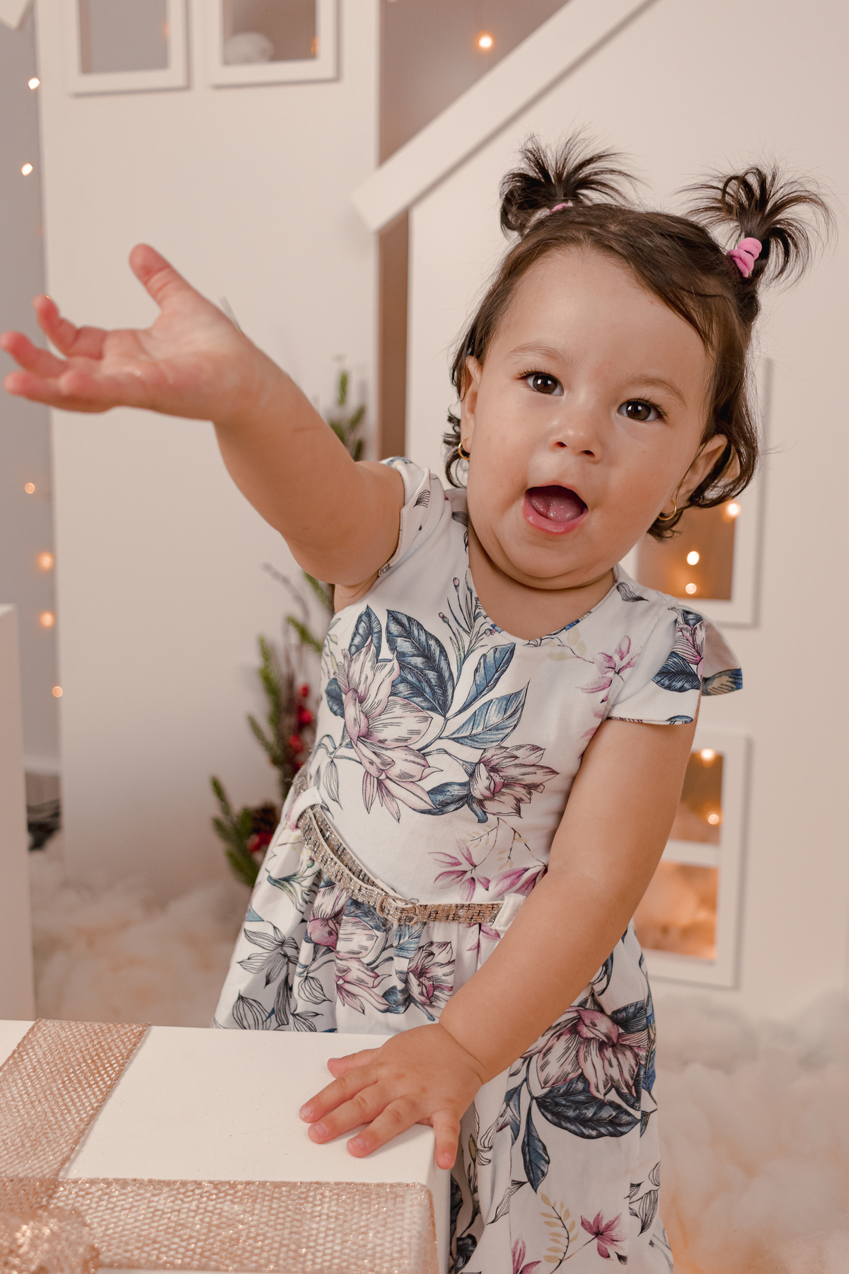 menina em frente cenario de natal com casinha e luzes. Menina olhando para a camera apontando pra frente
