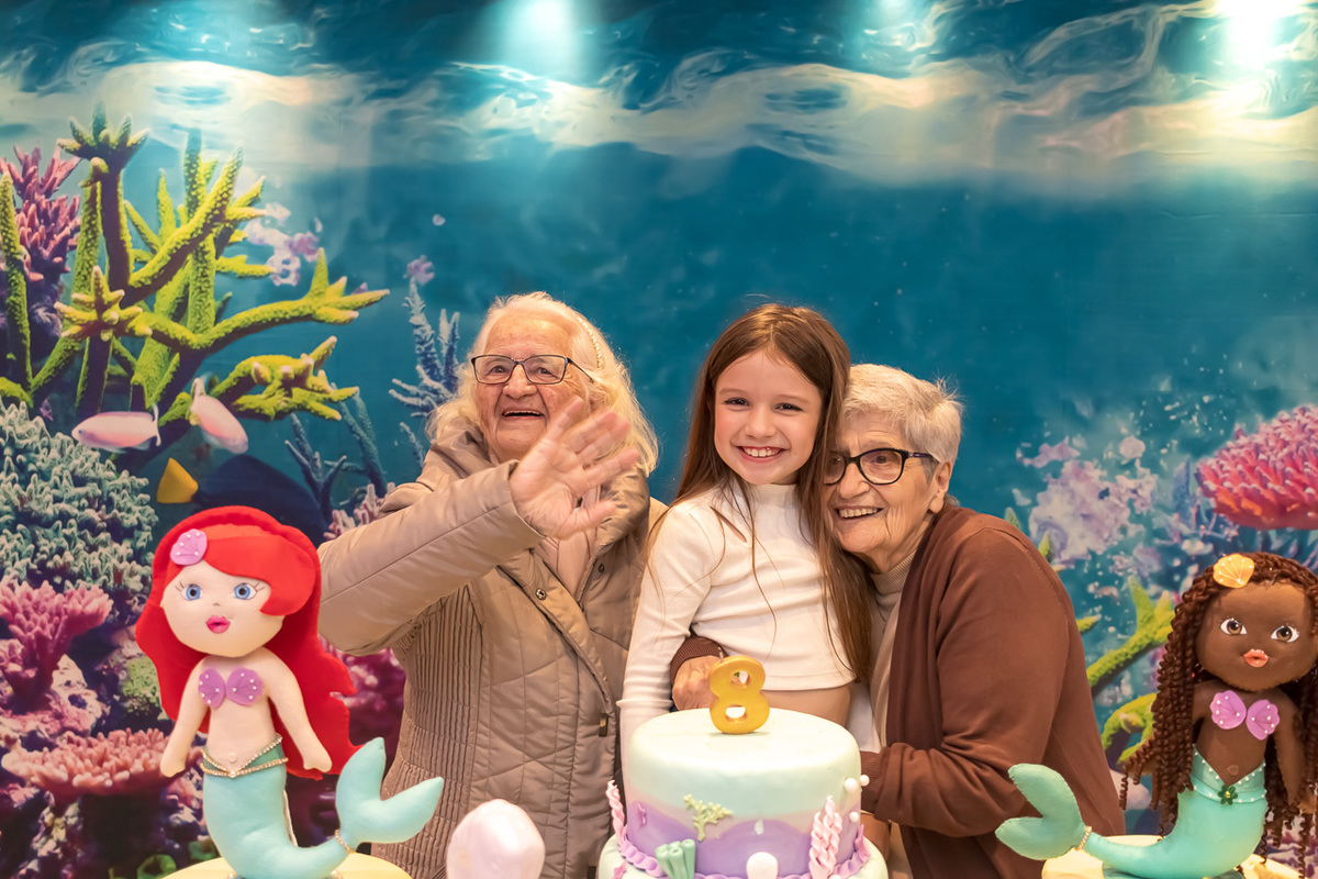 vovós e a neta no meio atrás da mesa com o bolo de aniversário