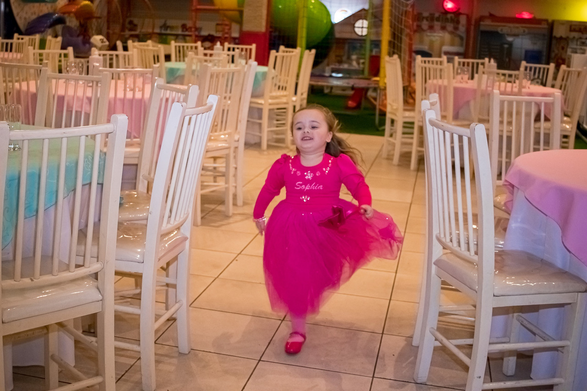 menina de vestido rosa de princesa correndo no meio das mesas