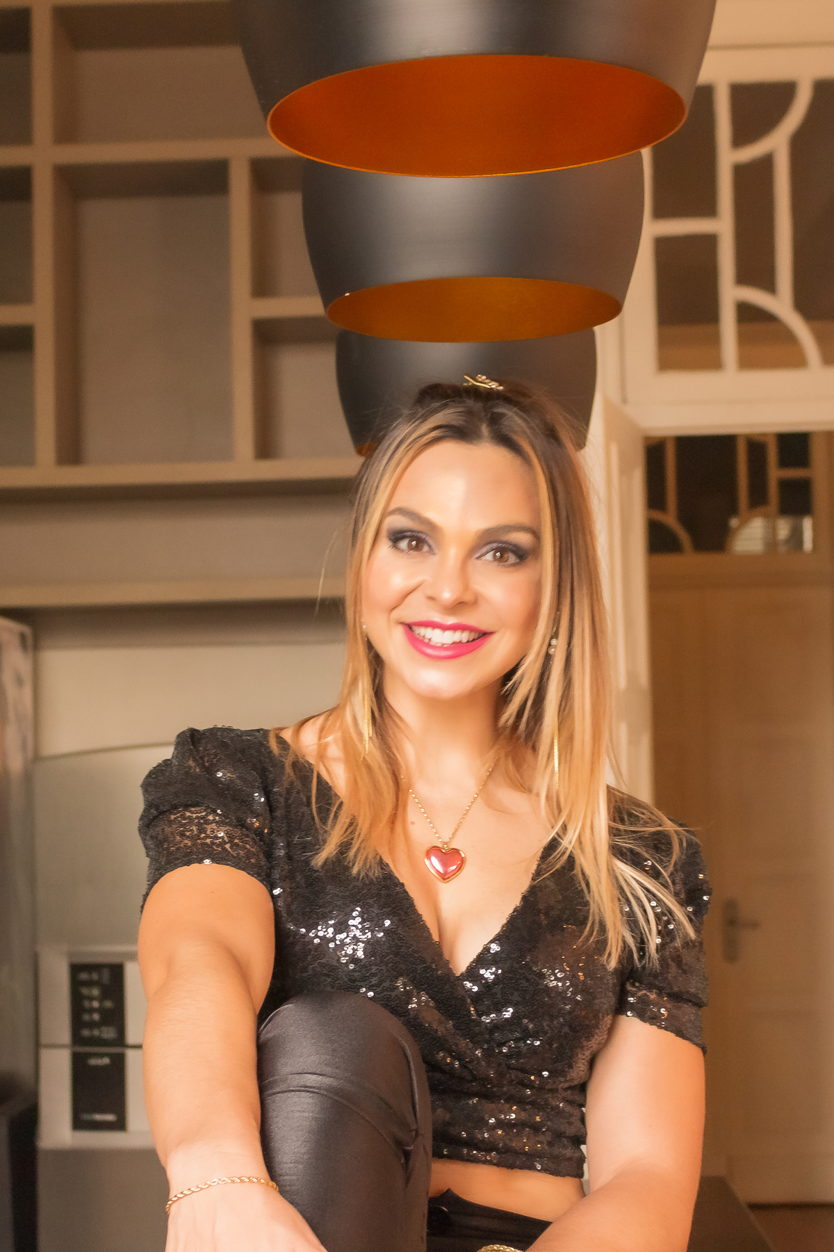 olhando direto para camera com sorriso fundo desfocado uma correntinha no pescoço com um coração rosa de pingente