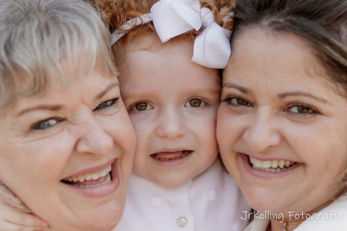 três meninas sorrindo. duas mulheres nas pontas encostando cabeça na cabeça da menina que está no meio