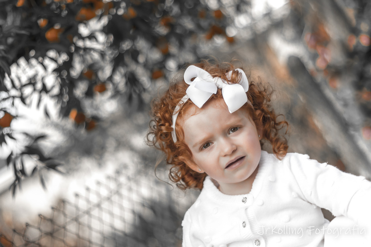 menina com cabelo ruivo esta em diagonal no canto inferior direto. Fundo desfocado, Imagem em tons de cinza com rosto e cabelo da menina mais alaranjado