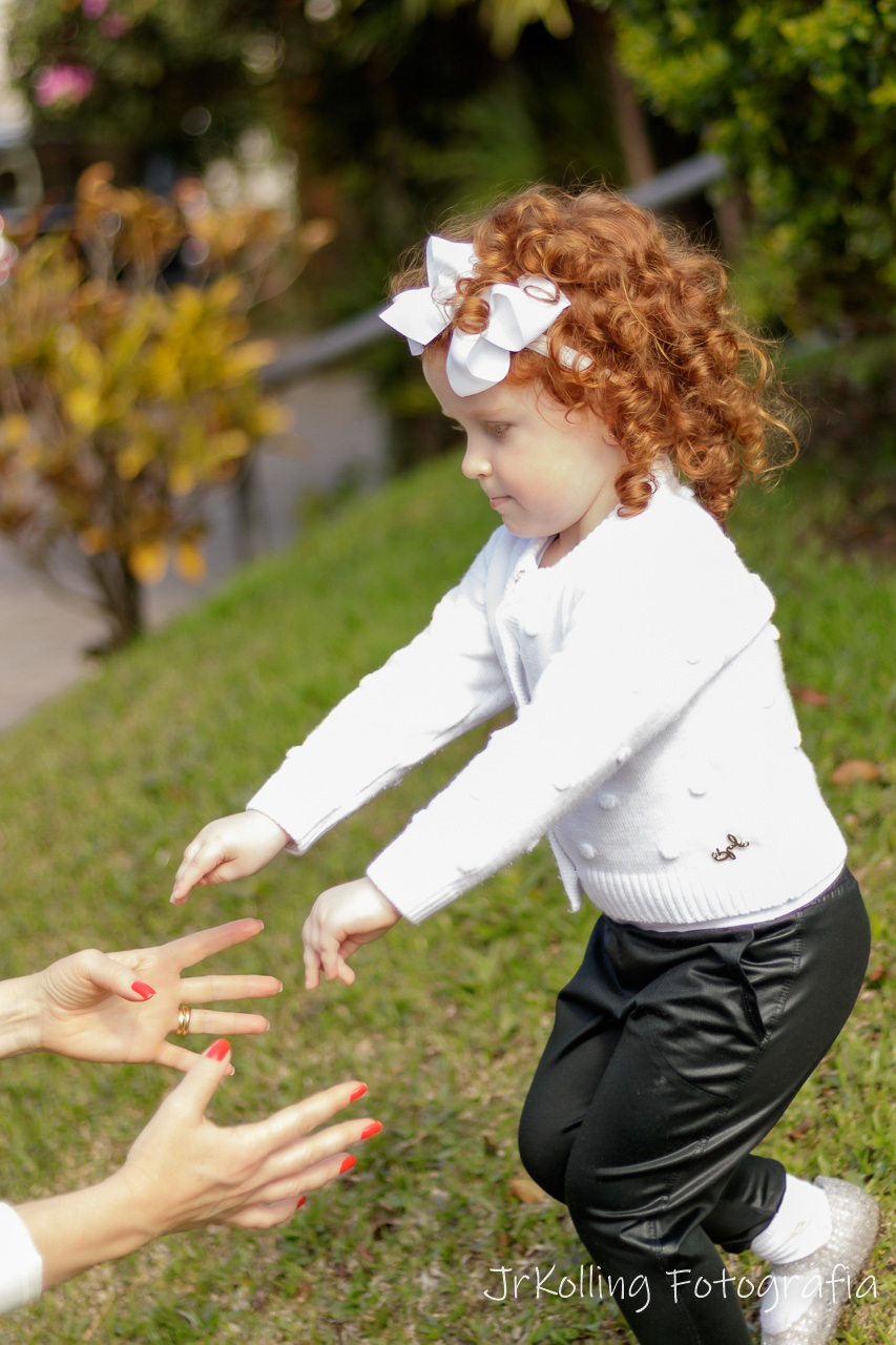 menina ruiva de camisa branca e calça preta com braço para frente em direção as mãos de uma mulher que esta fora de cena aparecendo somente as mãos a esquerda