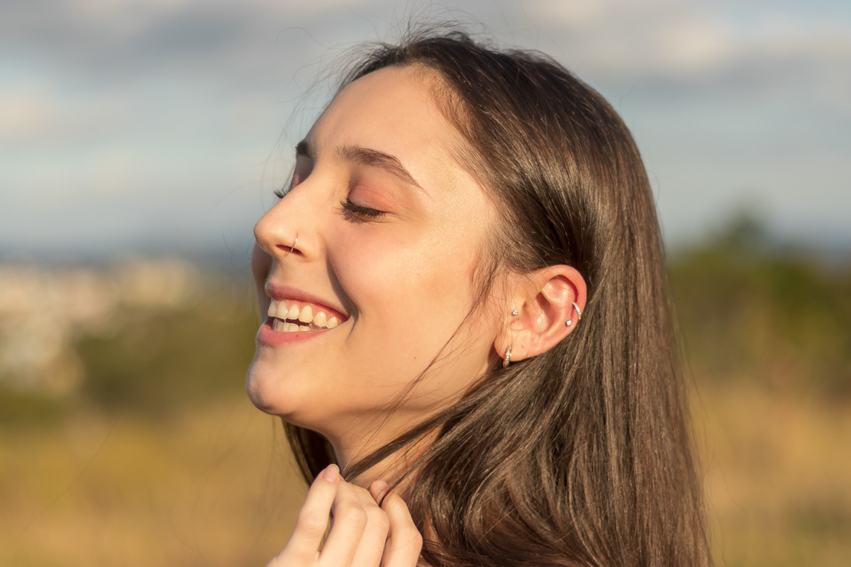 modelo passando mão no cabelo com cabeça levemente levantada e sorrindo com olhos fechados
