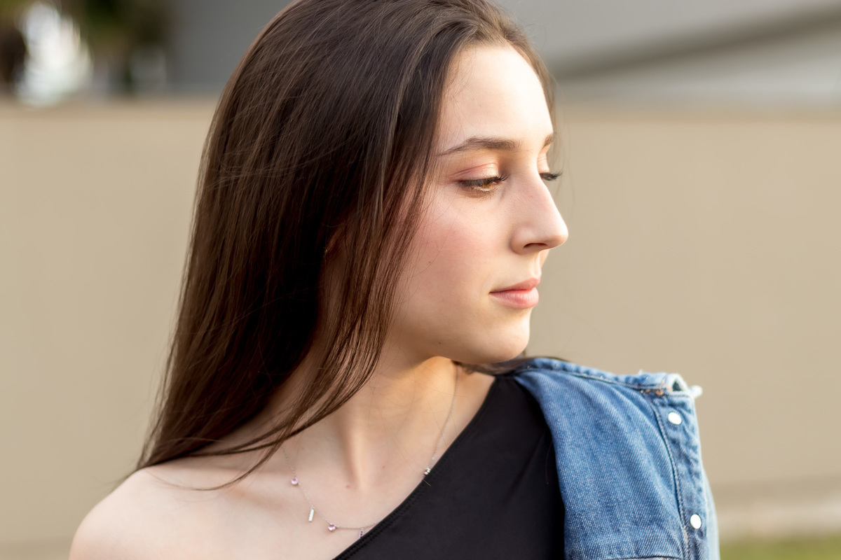 modelo olhando de lado. cabelo caído pelo lado do rosto. camisa com um ombro de fora