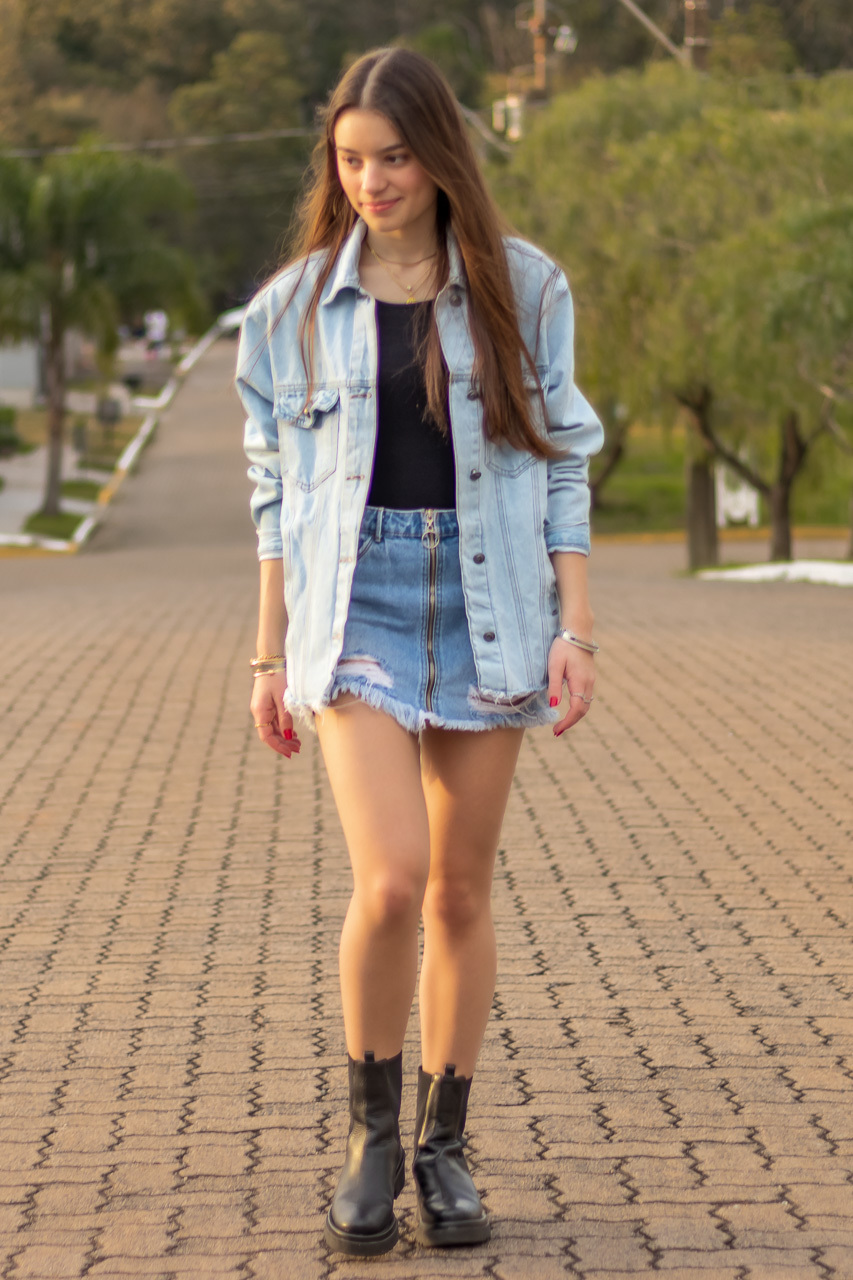 garota caminhando meio da rua de frente para a câmera usa blusa preta mini saia e jaqueta jeans