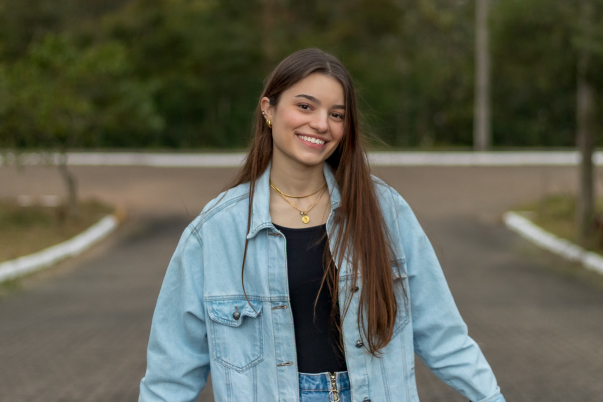 garota no meio da rua olhando de frente para a câmera fundo desfocado usando blusa preta e mini saia e jaqueta jeans