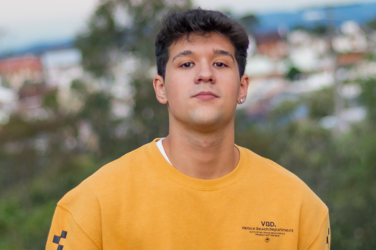 garoto com cabelo meio crespo olhando de frente para a lente. esta de moletom amarelo. aparecendo do peito para cima